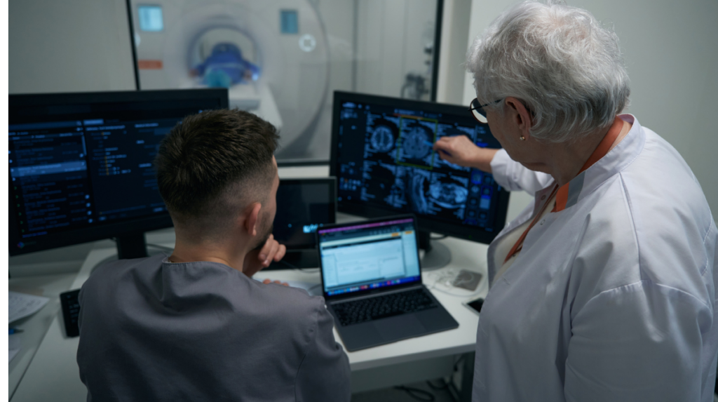 we see the backs of two healthcare professionals working together on a desk with several computers showing health information and data