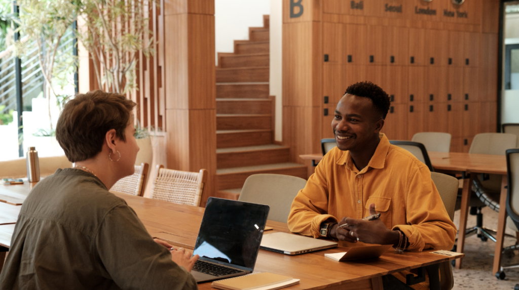 two individuals sit across from one another in a wood-walled office