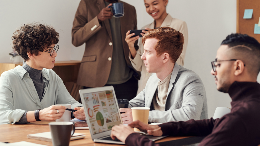 three people sit around a busy conference room in deep conversation