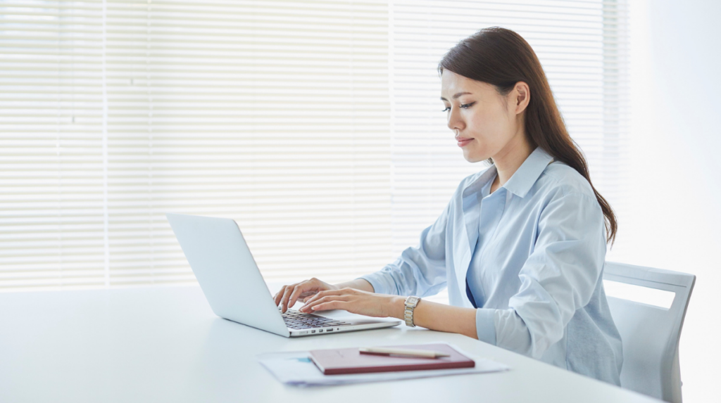 a woman sits at a desk with her hands on the keyboard of a laptop computer
