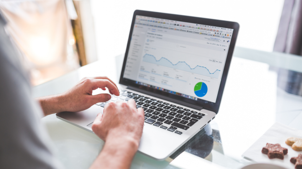 a person sits at a desk, their hands resting on a laptop keyboard while several charts and graphs appear on the computer screen