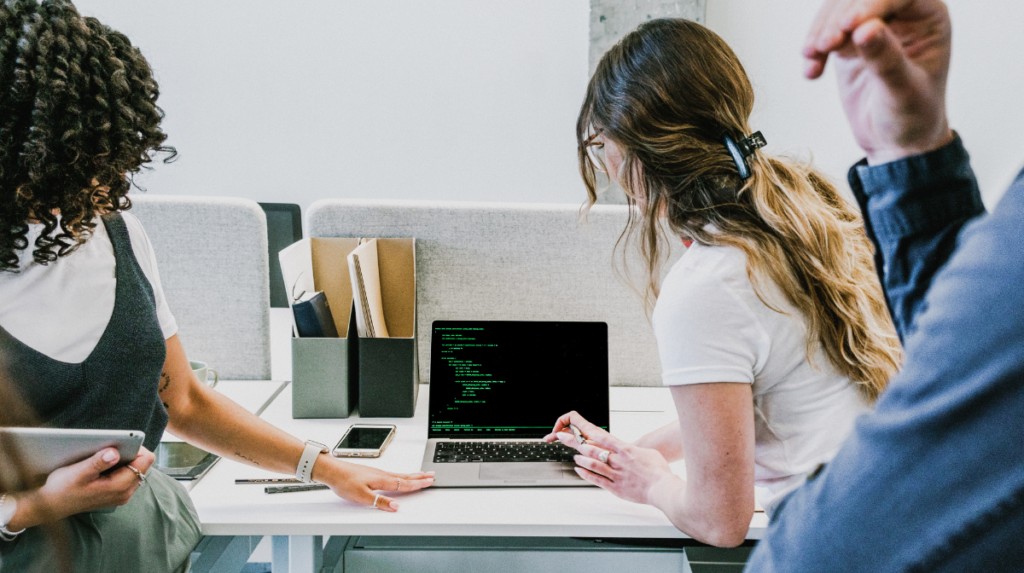 several individuals look at the same computer screen together, featuring coding language