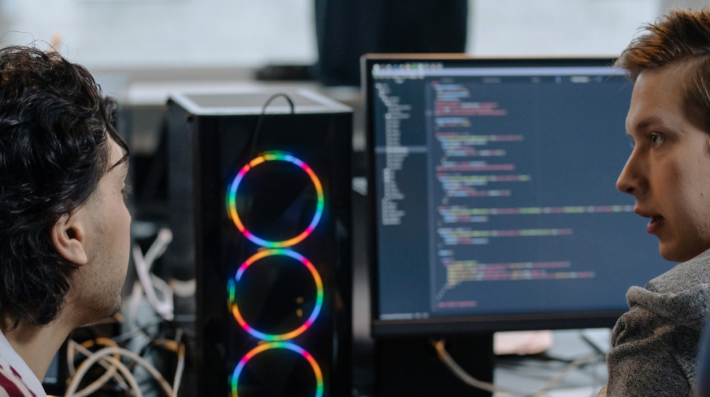 two individuals sit in front of two computer screens deep in conversation
