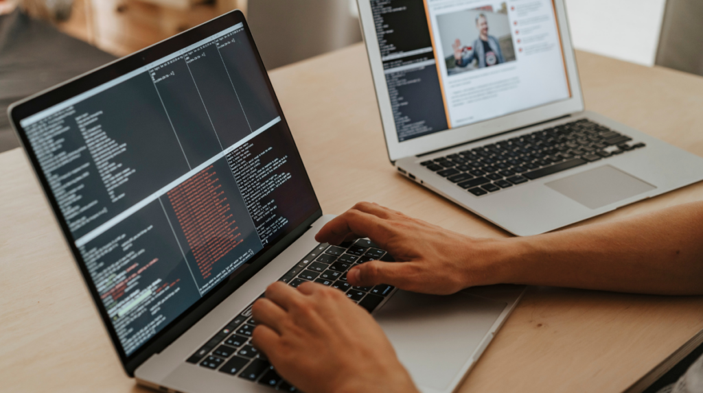 two hands type on the keyboard of a laptop displaying coding language