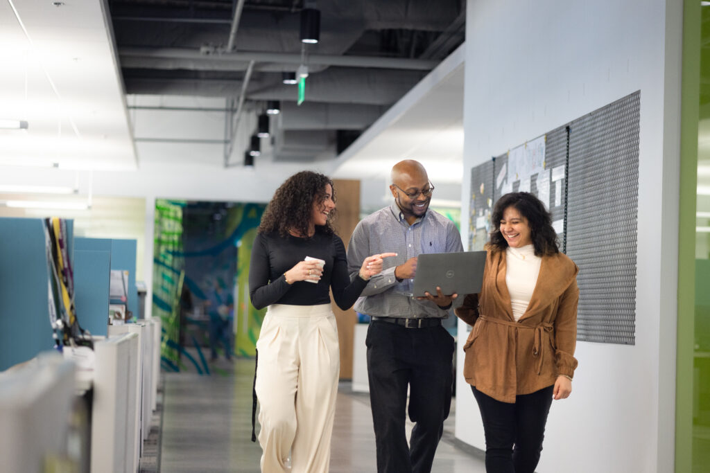 three individuals walk down a hallway together in a professional office setting in discussion
