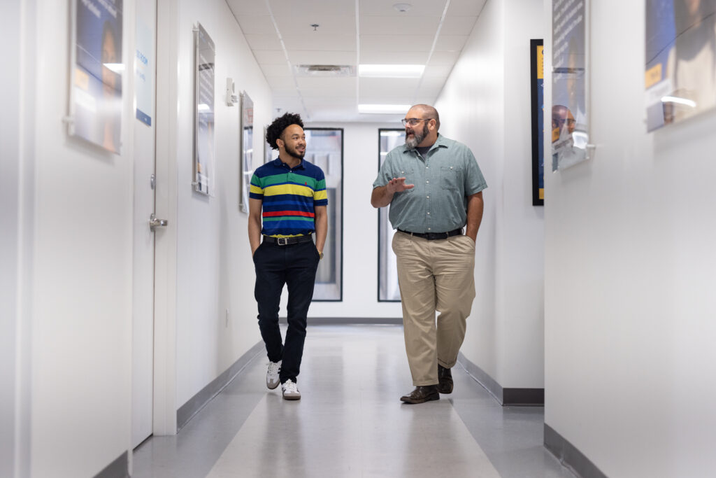 two gentlemen walk down a hallway together in conversation