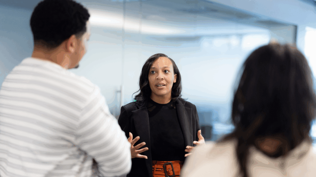a woman stands facing two other office workers engaged in conversation