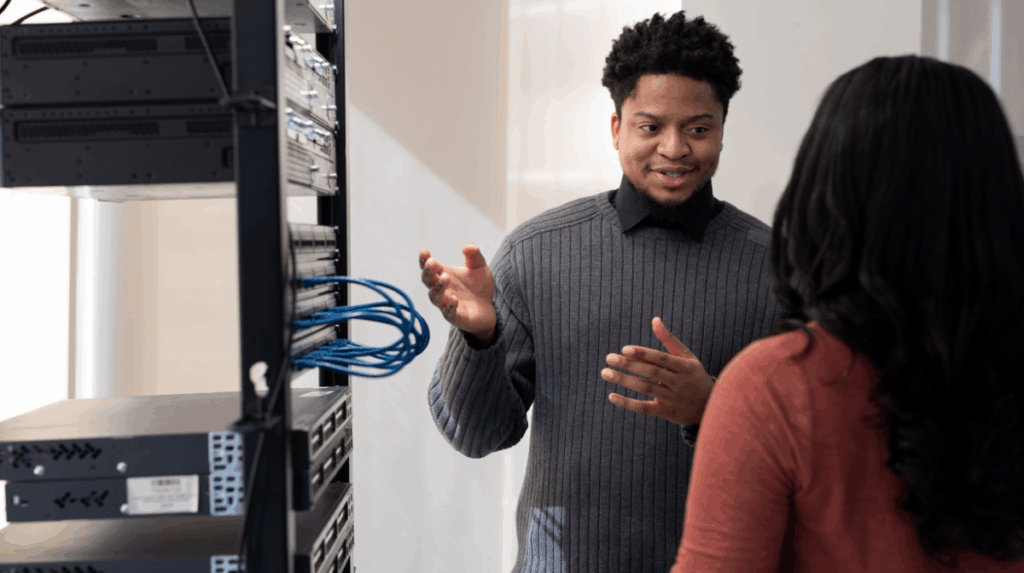 two individuals stand in front of a server tower, in an active discussion