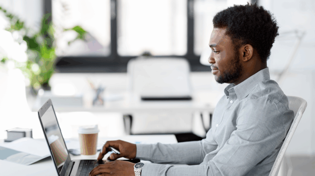 a black man sits at a desk in profile, looking at a computer and typing on the keyboard
