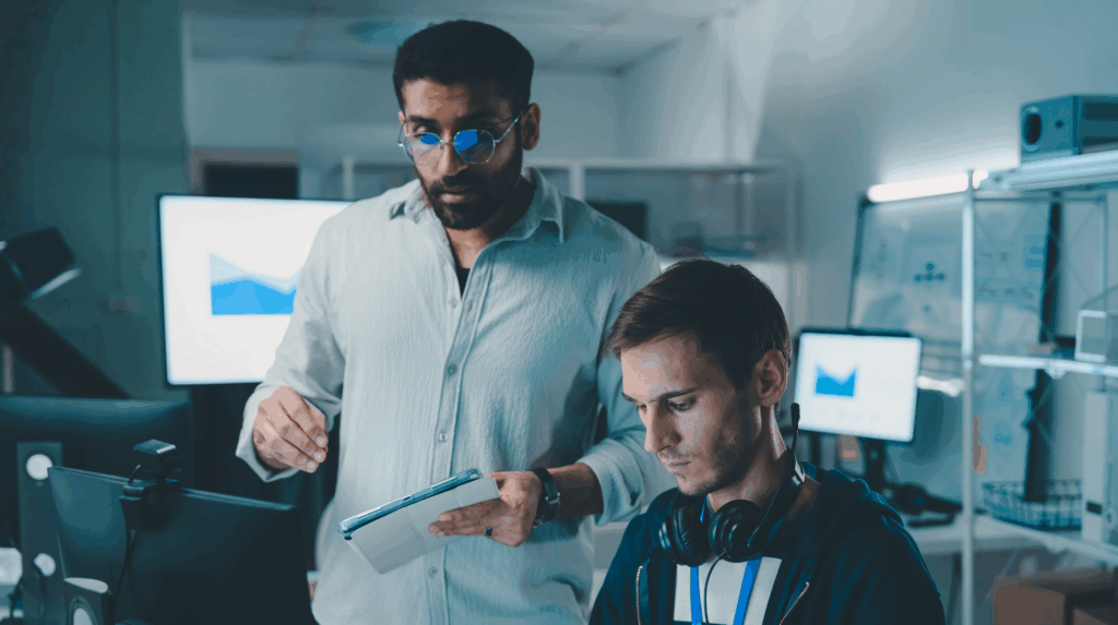 Two colleagues collaborating at a workstation while reviewing information on a tablet