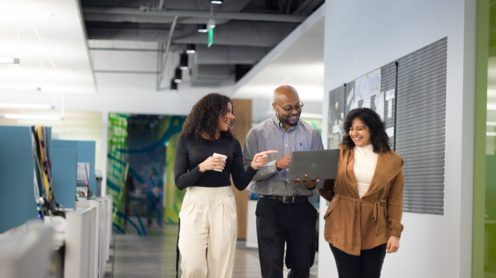 Team reviewing information on a laptop, walking down the hallway of an office