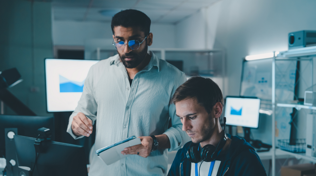 Two coworkers reviewing data on a screen beside computer screens showing charts.