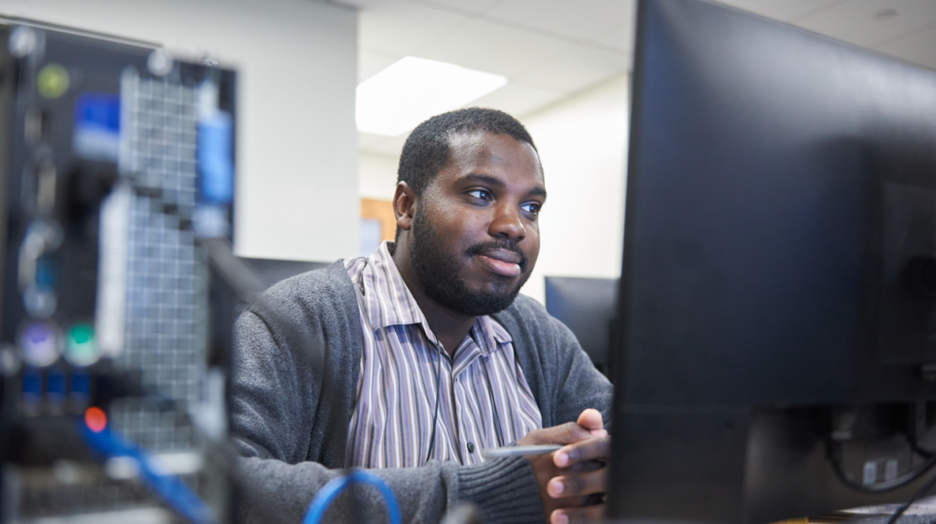 A cybersecurity technologist sits in front of a monitor with a desktop computer in the foreground