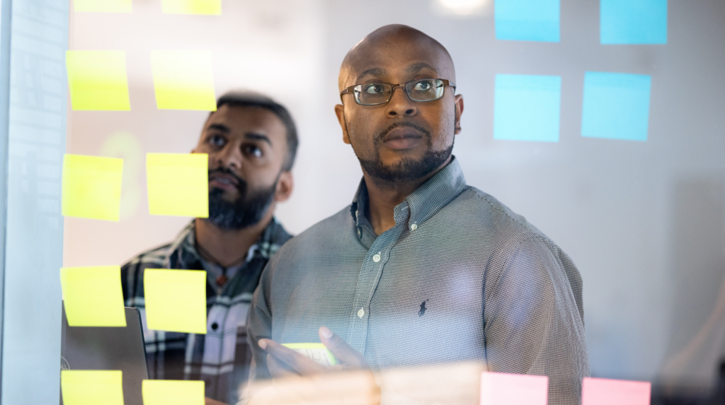 Two IT leaders reviewing sticky notes on a wall during a planning session.
