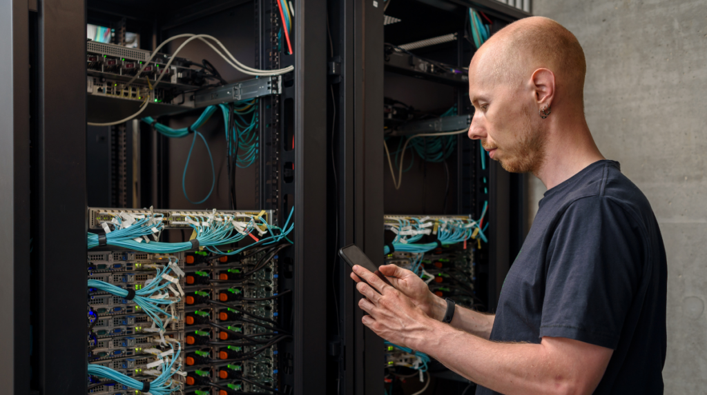 Male technician auditing fiber cabling and network connections inside a server rack
