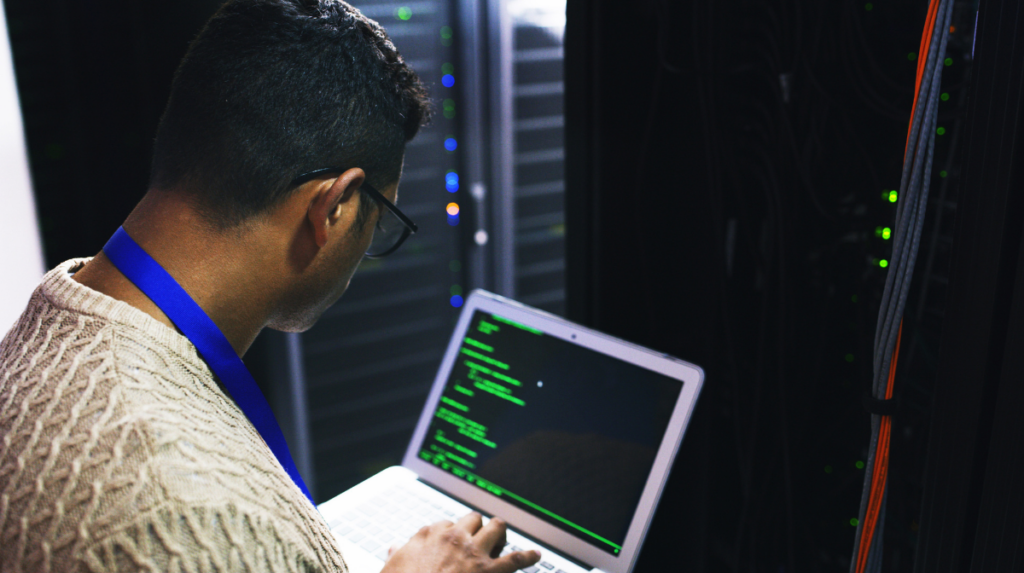 Cybersecurity technician reviewing code on a laptop in front of a server rack