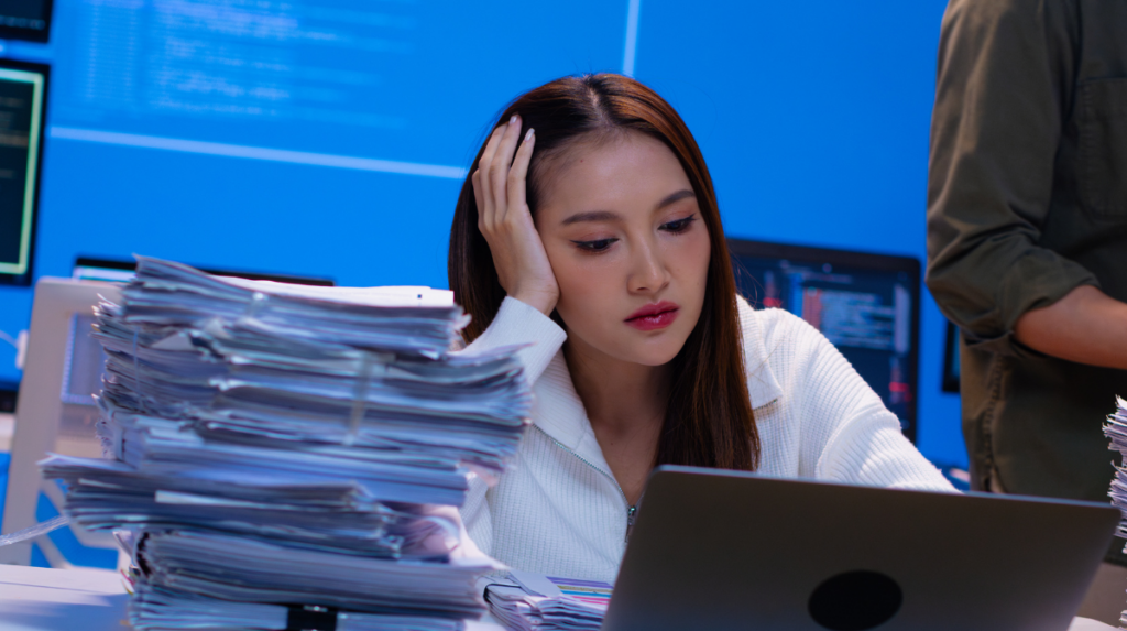 Overwhelmed cybersecurity professional surrounded by documents in an understaffed security operations center